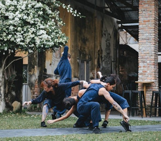 Group of dancers in blue costumes perform outdoors by an old building.